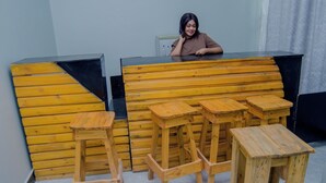 Ένα ξύλινο παγκάκι και σκαμπό σε ένα δωμάτιο με γκρι τοίχο και λευκό κουρτίνα.