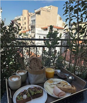 Un plateau de petit-déjeuner sur un balcon, avec du café, des toasts, des œufs et des viennoiseries.