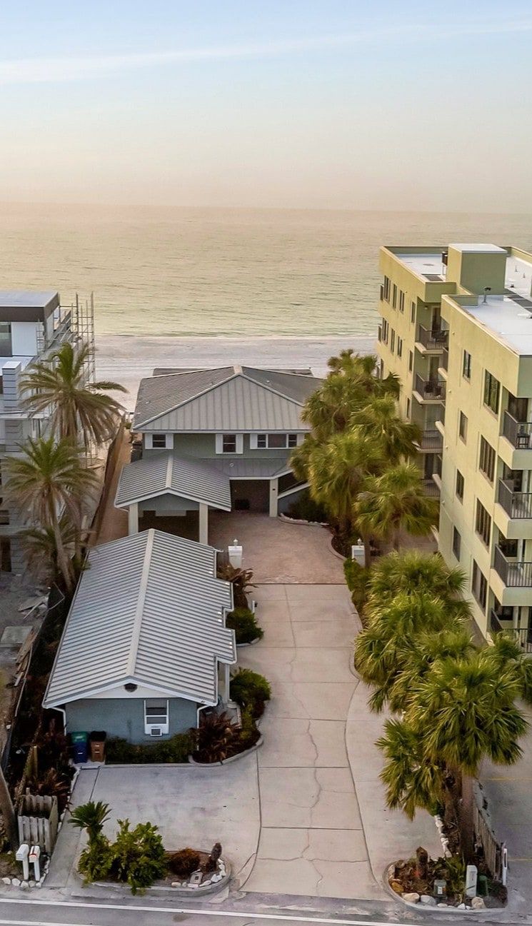 This beachfront property sits steps from the sand, with palm trees and nearby coastal buildings framing the serene ocean waters at golden hour.