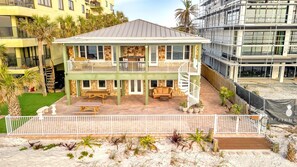 A two-story building with a balcony, outdoor seating, and a sandy area with plants.