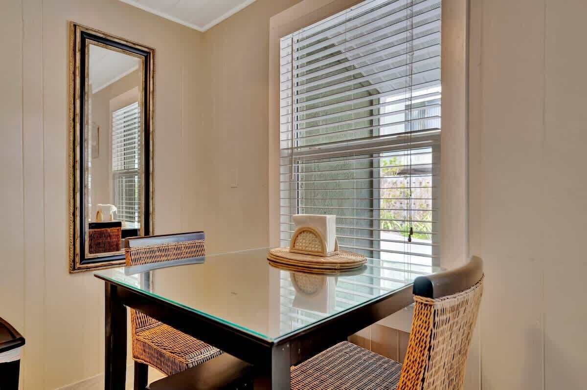 A dining area with a glass table, wicker chairs, a mirror, and a window with blinds.