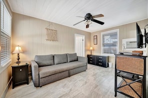 A living room with a sofa, a small table, a ceiling fan, and a television.