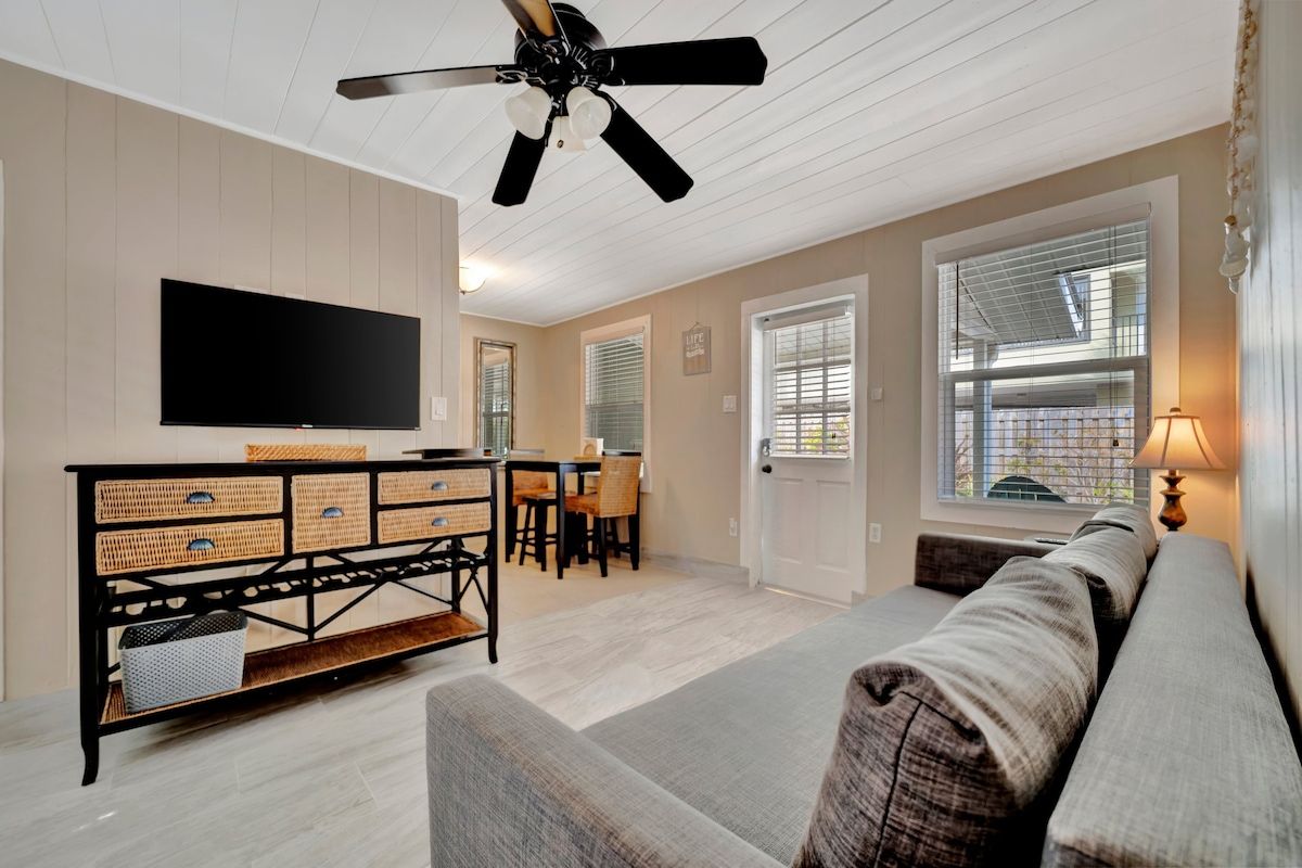 Ein Wohnzimmer mit Flachbildfernseher, Deckenventilator, Essbereich mit Tisch und Stühlen sowie einer Couch.