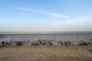 A balcony with a view of the beach, a metal railing, and a tiled floor.