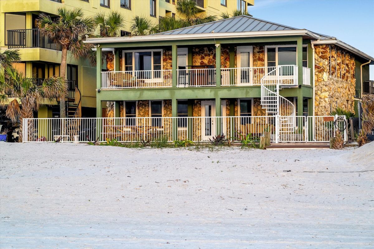 A multi-story building with balconies, a staircase, and a sandy foreground.