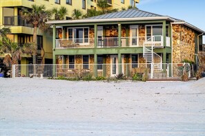 A multi-story building with balconies, a staircase, and a sandy foreground.