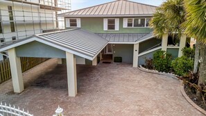 Een tweelaags huis met een overdekte patio, een omheind erf en een kleine tuin met planten en een palmboom.