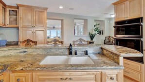 A kitchen with granite countertops, wooden cabinets, a double sink, and a built-in oven. - Relax on the Beach! Private Balcony Oceanview (Indian Rocks Beach)