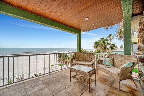 A balcony with wicker furniture, a view of the beach, and a railing.