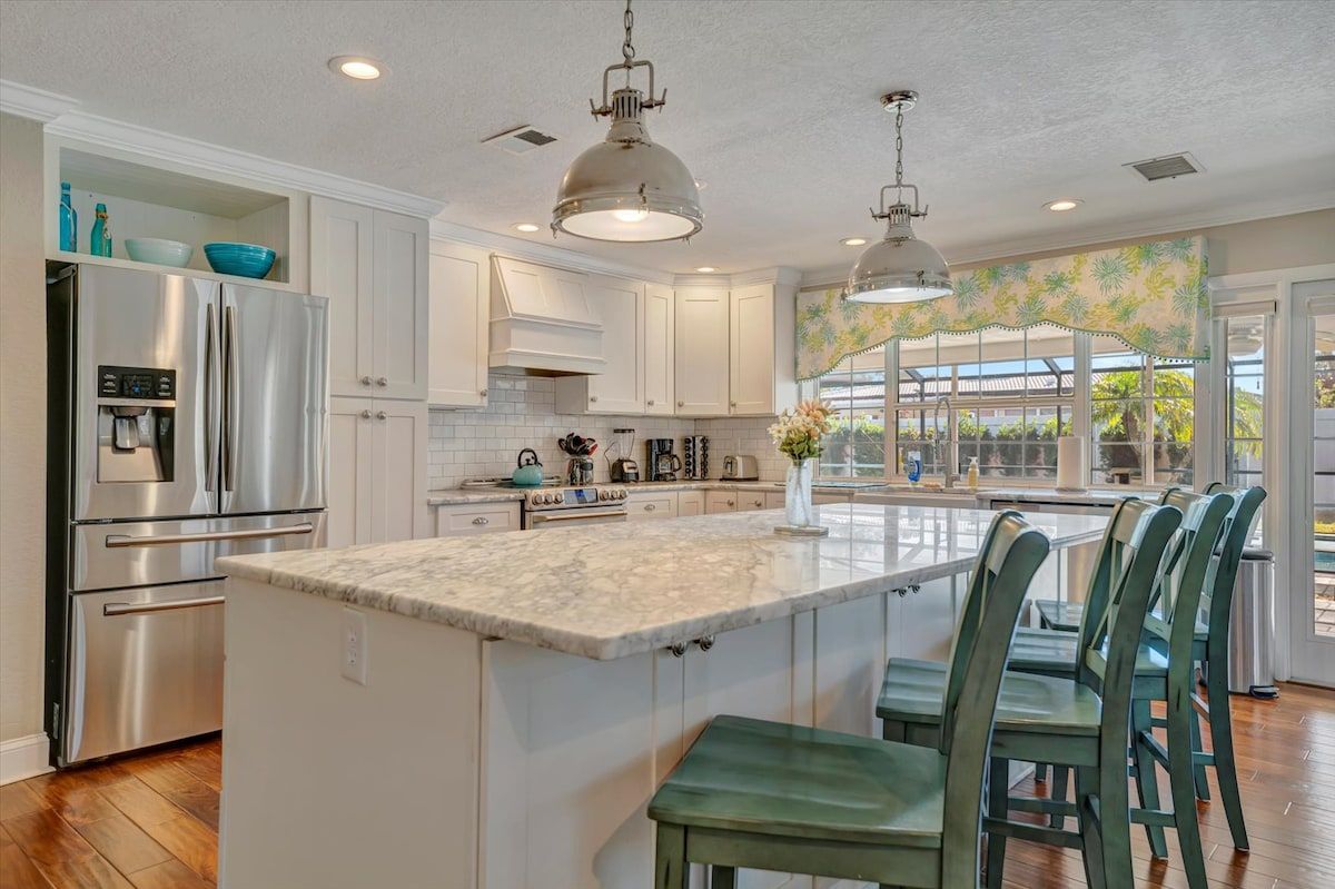 A kitchen with a central island, stainless steel appliances, and a view to the outside.