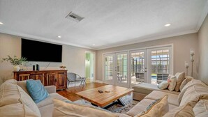 A spacious living room with a large flat-screen TV, a wooden coffee table, and a beige sofa.
