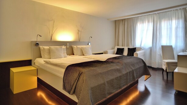 A modern hotel room with a large bed, bedside tables, a desk, and a chair.