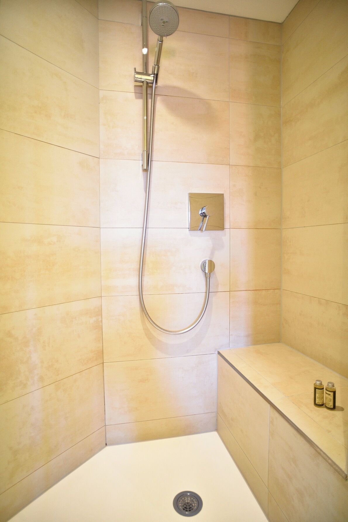 Douchehoek met een handdouche, bedieningspaneel aan de muur en een klein plankje met flessen.