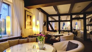 A well-lit, modern hotel lobby with a round dining table, comfortable seating, and large windows allowing natural light.
