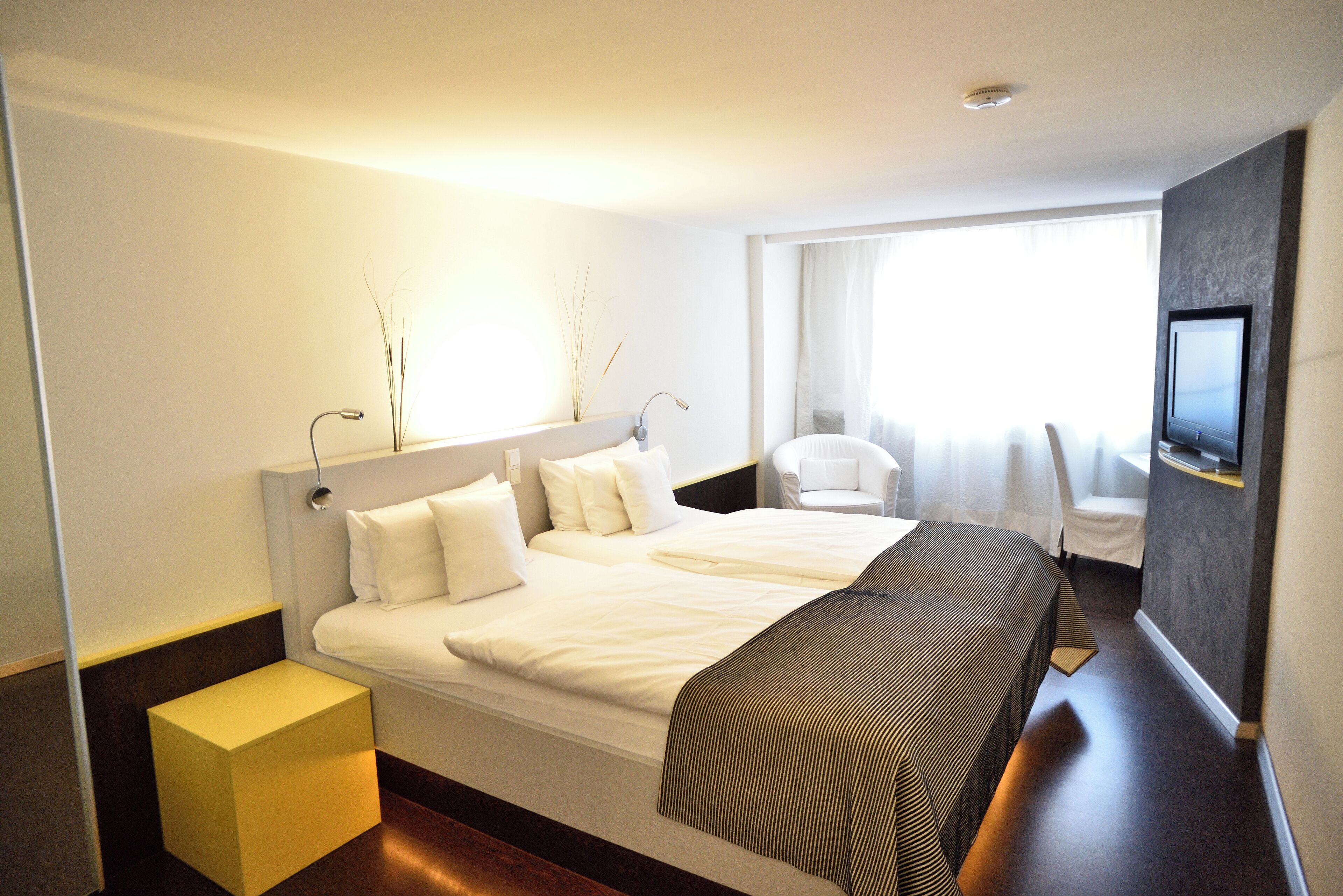 Een moderne hotelkamer met een groot bed, een nachtkastje, een televisie en een raam met gordijnen.