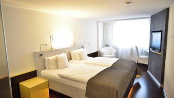 A modern hotel room with a large bed, a bedside table, a TV, and a window with curtains.