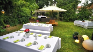 An outdoor dining area with tables set for a meal, surrounded by greenery.