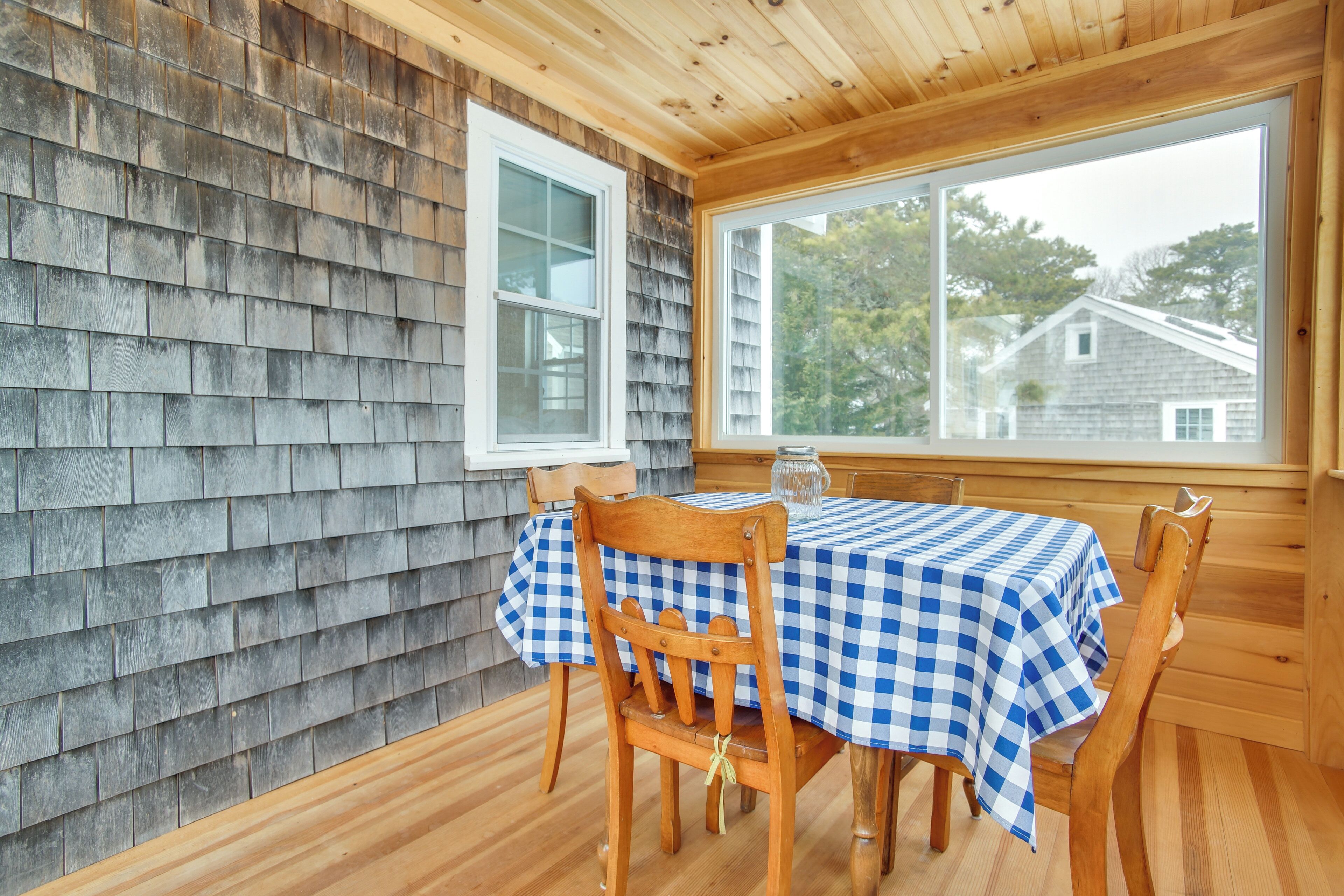 Comedor con una mesa dispuesta para cuatro personas, paredes de madera y una ventana con vista a casas.
