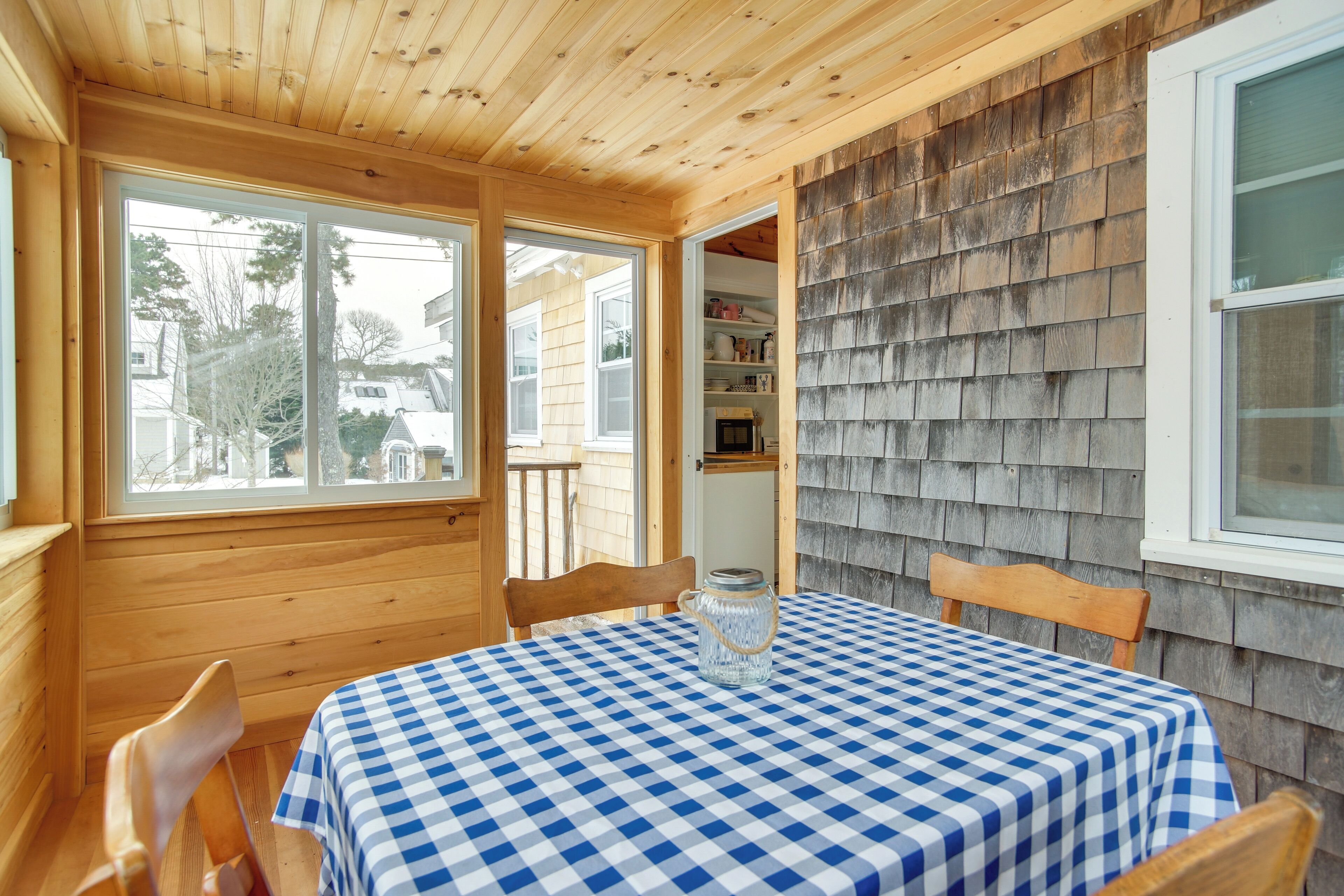 A wooden interior with a checkered tablecloth, wooden chairs, and a view through a window.
