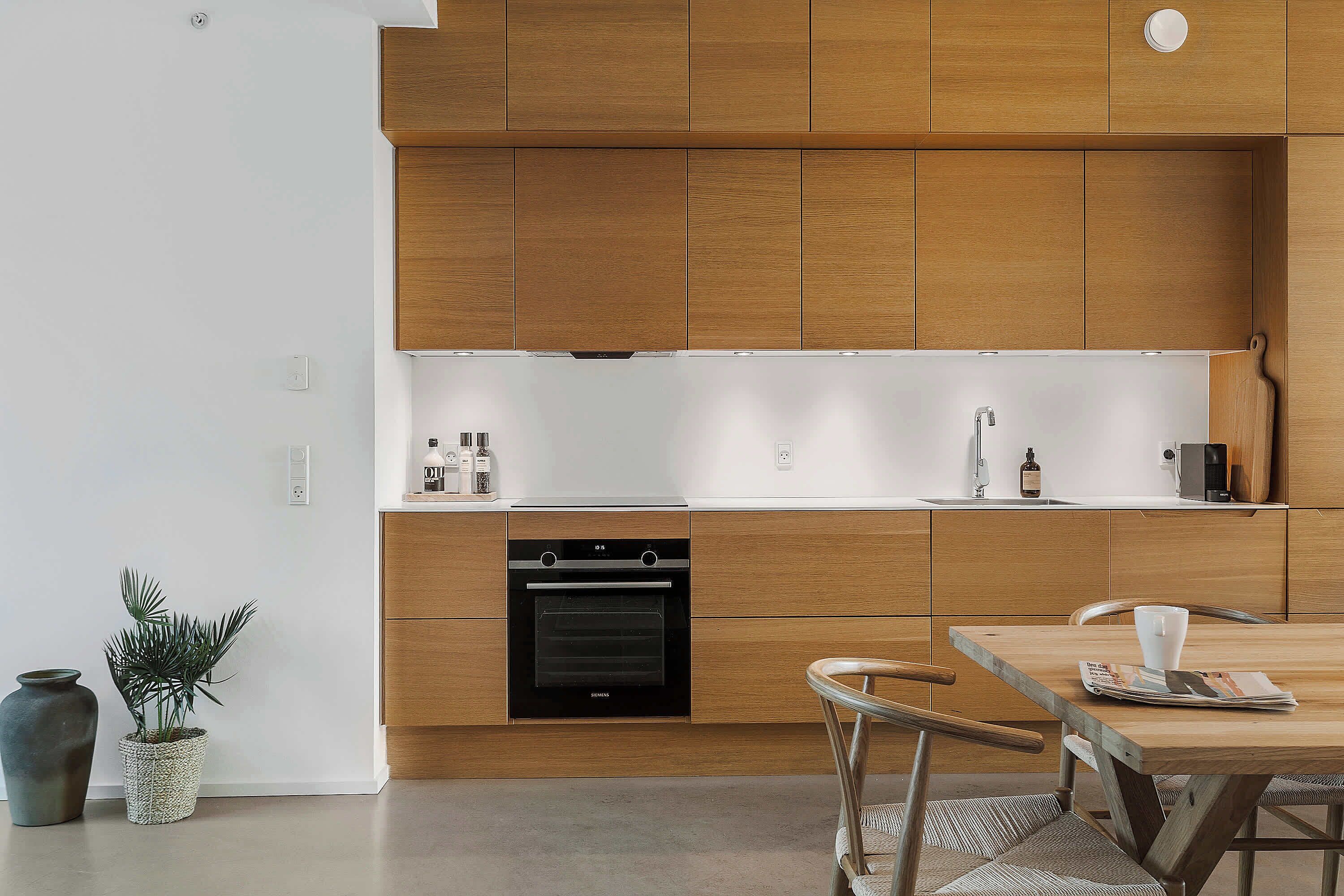 A modern kitchen with wooden cabinets, a built-in oven, and a dining area with a table and chairs.