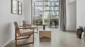 Un salon moderne avec une grande fenêtre, deux tableaux encadrés, une table basse en bois et deux fauteuils.