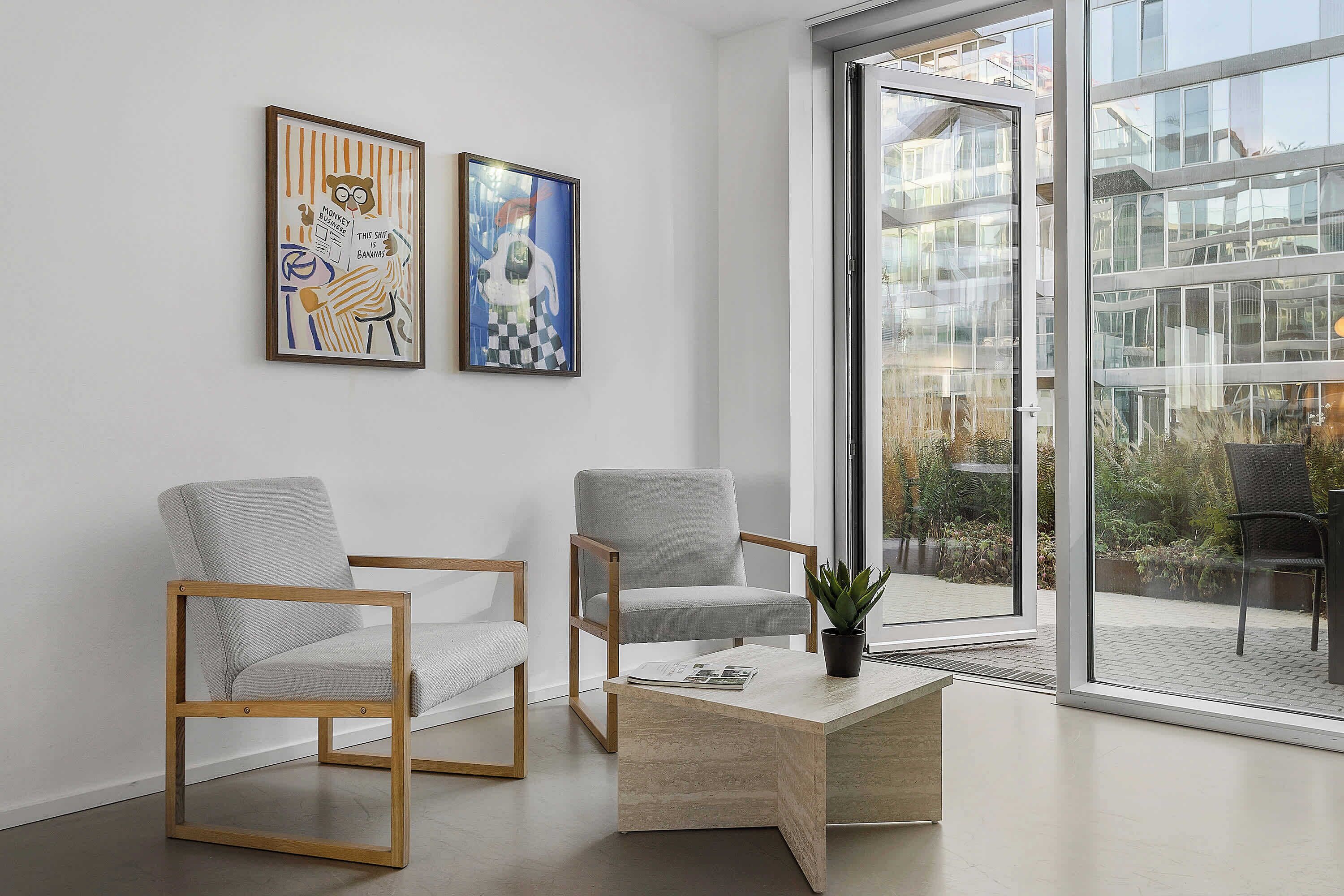 Ein modernes Interieur mit zwei grauen Sesseln, einem Holztisch und zwei gerahmten Kunstwerken an der Wand.