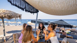 A group of people toasting at a table with a view of the beach and ocean. - Zen Suites & Spa (Santorini)
