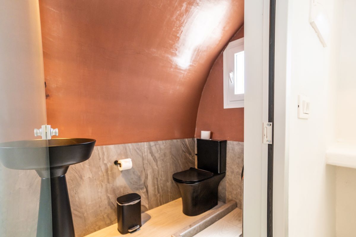 A compact bathroom with a modern design, featuring a pedestal sink, a black toilet, and a trash bin.