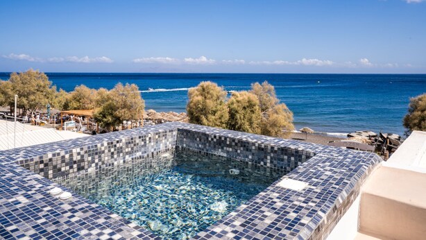 A swimming pool with a tiled edge, overlooking a beach and the sea. - Zen Suites & Spa (Santorini)