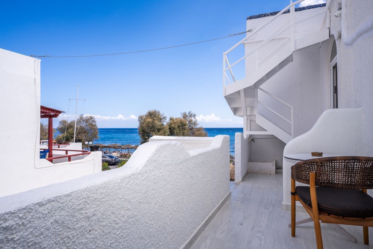 Un balcon avec vue sur la mer, une chaise en osier et un bâtiment blanc.