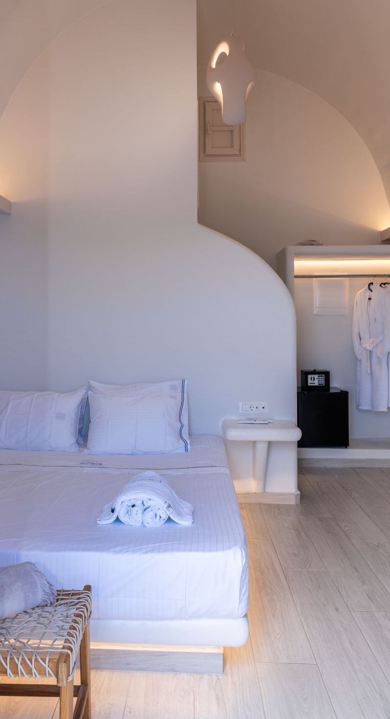 A modern hotel room with a large bed, bedside tables, a seating area, and a robe hanging on the wall.