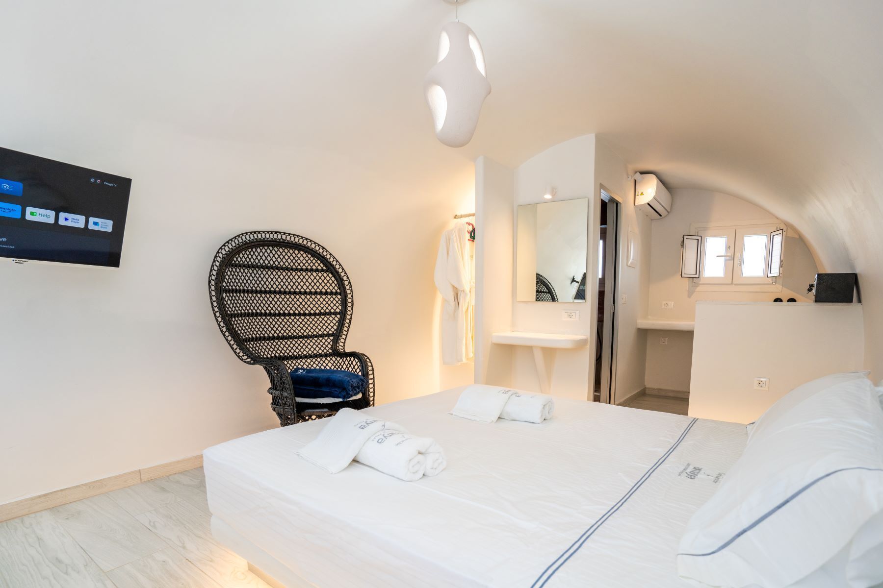 A hotel room with a bed, a chair, a TV, a mirror, and a bathroom.
