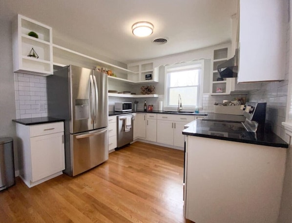 A modern kitchen with white cabinetry, stainless steel appliances, and a wooden floor.