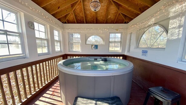 Un jacuzzi en un espacio exterior cubierto con techo de madera, una banca y un taburete pequeño.