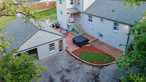 A two-story house with a backyard containing a small putting green and a patio area with outdoor furniture.