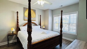 A four-poster bed with a quilted white bedspread, two bedside tables with lamps, a ceiling fan, and a window with blinds. - Memorable stay at cozy 2BR condo in Magnolia (Myrtle Beach)