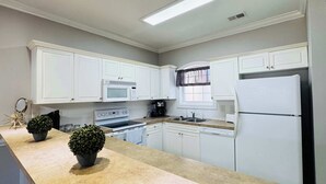 A kitchen with white cabinets, a microwave, stove, refrigerator, and a window with curtains. - Memorable stay at cozy 2BR condo in Magnolia (Myrtle Beach)