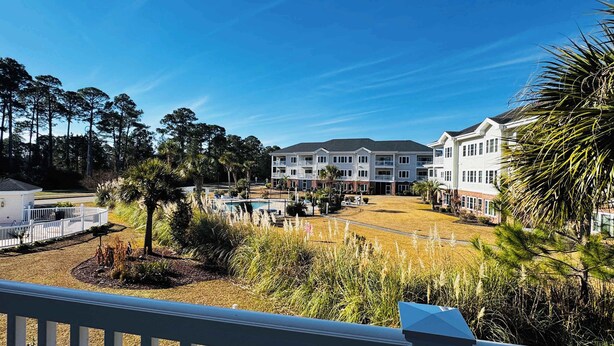 A multi-story hotel with a swimming pool, surrounded by trees and a well-maintained lawn. - Memorable stay at cozy 2BR condo in Magnolia (Myrtle Beach)