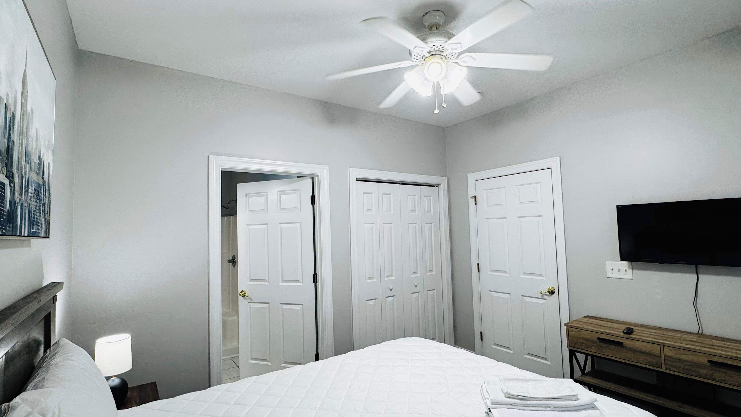A bedroom with a bed, a ceiling fan, a TV, and two doors.