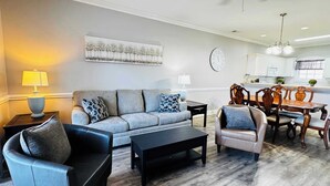 A modern living room with a grey sofa, black coffee table, and leather armchairs. A dining area with wooden chairs and a table is visible. - Memorable stay at cozy 2BR condo in Magnolia (Myrtle Beach)