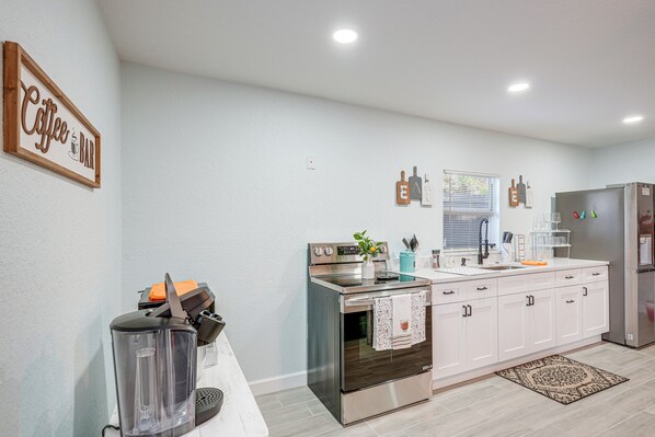 A modern kitchen with white cabinets, stainless steel appliances, and a coffee bar sign. - Vibrant Tampa Home: Perfect for Long Stays! (Lutz)