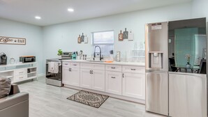 A modern kitchen with white cabinets, a built-in oven, and a refrigerator. There is a coffee bar on the left and a window with blinds. - Vibrant Tampa Home: Perfect for Long Stays! (Lutz)