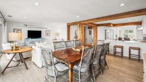 A modern living room with a dining area, wooden beams, a flat-screen TV, and a kitchen with white cabinets. - 632 Newhaven (Fripp Island)