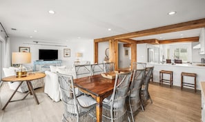 A modern living room with a dining area, wooden beams, a flat-screen TV, and a kitchen with white cabinets. - 632 Newhaven (Fripp Island)
