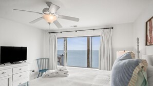 A hotel room with a bed, a television, a chair, a balcony with a view of the sea, and a ceiling fan. - 632 Newhaven (Fripp Island)