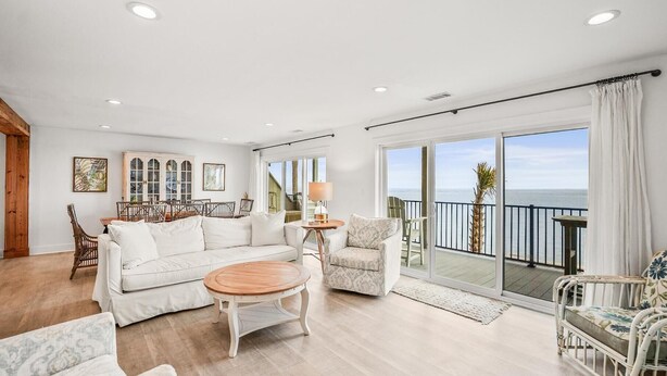 A spacious living room with a white sofa, a wooden coffee table, and a balcony with a view of the sea. - 632 Newhaven (Fripp Island)