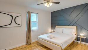 A bedroom with a bed, a ceiling fan, a window with curtains, and a wall with a geometric design.