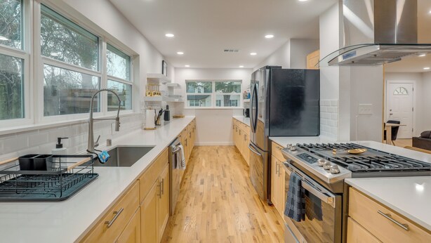 A modern kitchen with a central island, stainless steel appliances, and large windows.