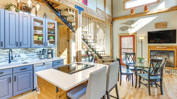 A modern kitchen with a central island, wooden beams, and a staircase leading to an upper level.