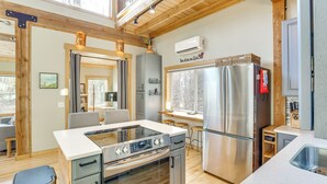 A modern kitchen with a central island, stainless steel appliances, and a wooden ceiling.